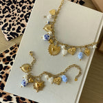 Vue à plat de l'ensemble collier et bracelet en acier inoxydable doré avec breloques cœurs et perles bleues, présentés avec pochettes cadeau léopard.