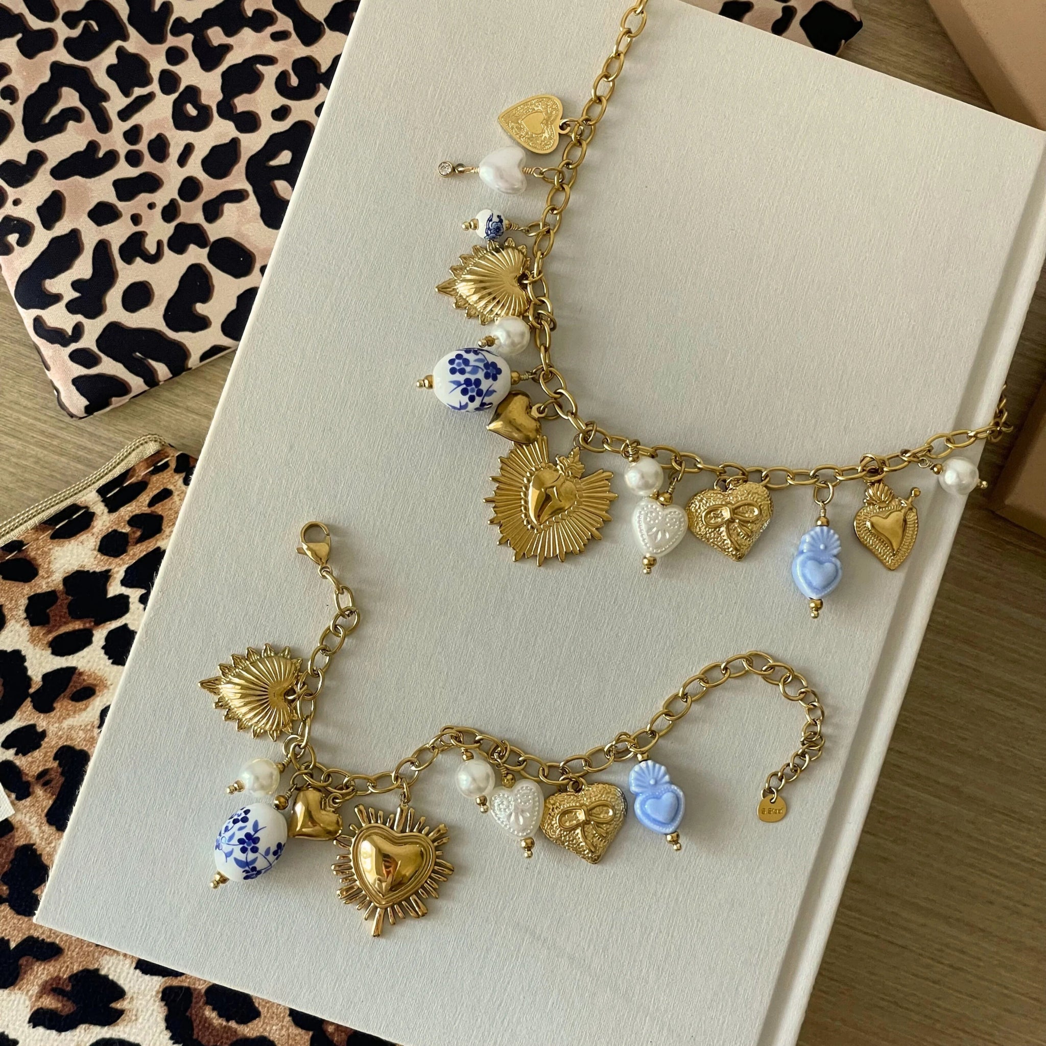 Vue à plat de l'ensemble collier et bracelet en acier inoxydable doré avec breloques cœurs et perles bleues, présentés avec pochettes cadeau léopard.