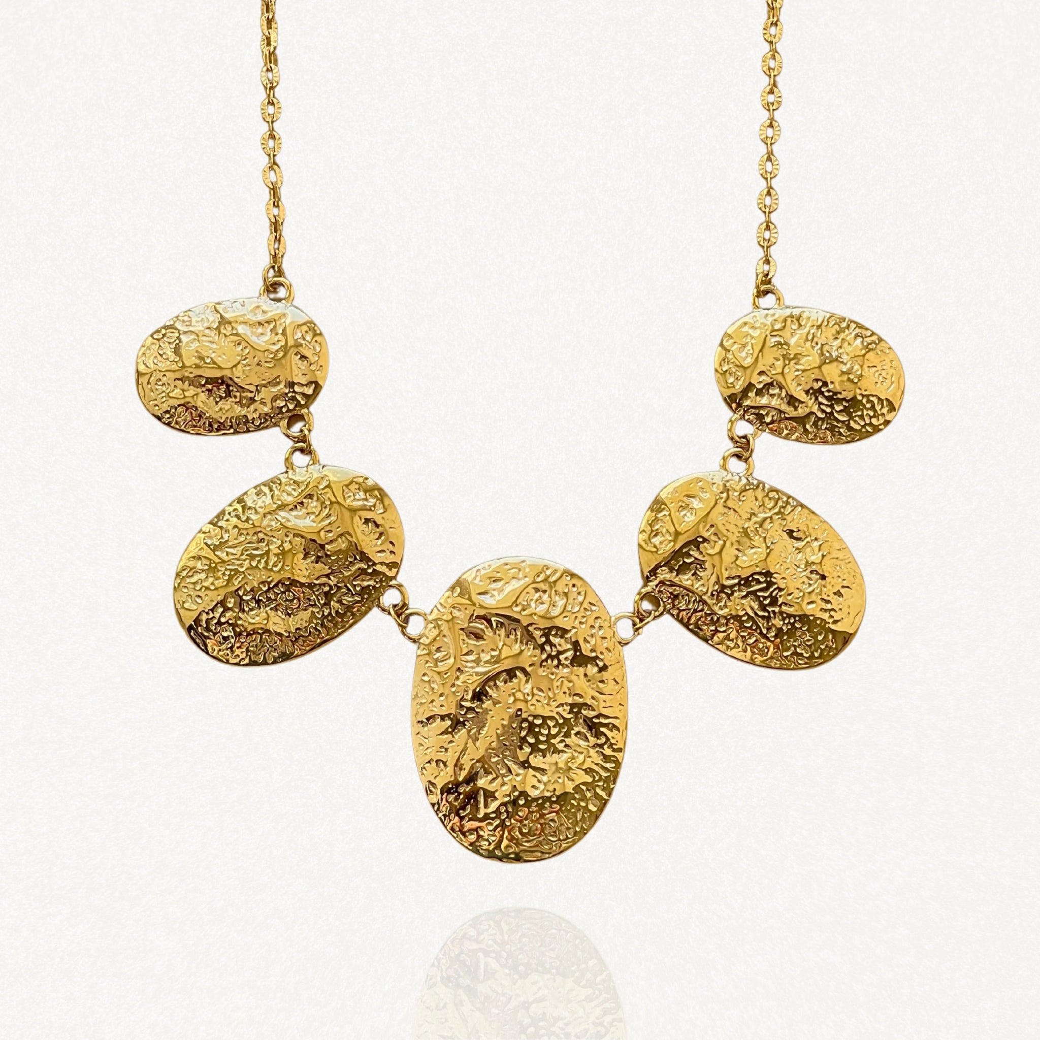 Vue d'ensemble collier chaîne dorée avec 5 pendentifs ovales finition irrégulière et texturée sur fond blanc.
