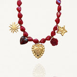 Vue d'ensemble collier perles rouges avec pendentif central cœur ex-voto et charms rose et célestes sur fond blanc.