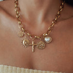 Collier grosse maille en acier inoxydable doré avec multiples breloques : croix, soleil, médailles et cœur perlé.