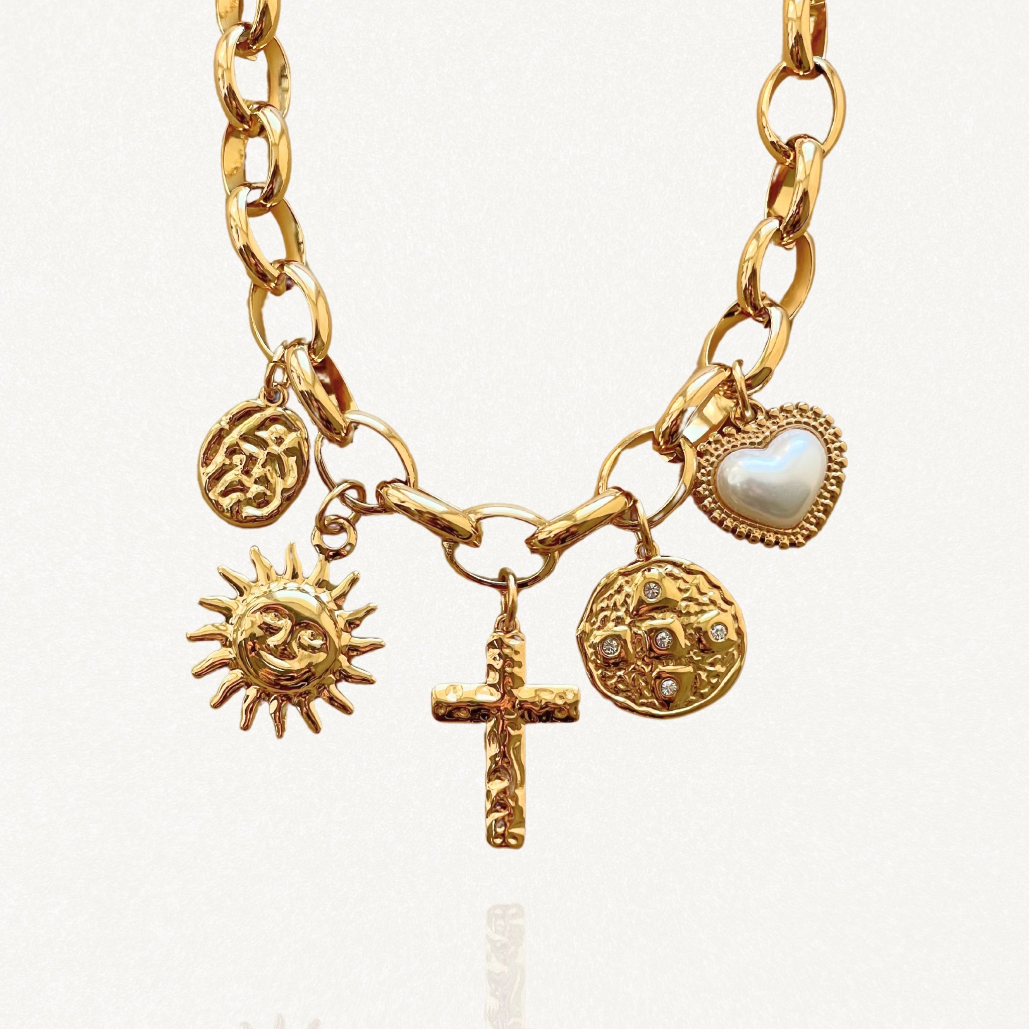 Gros plan sur les pendentifs du collier : croix centrale, soleil visage, médailles texturées et cœur blanc.