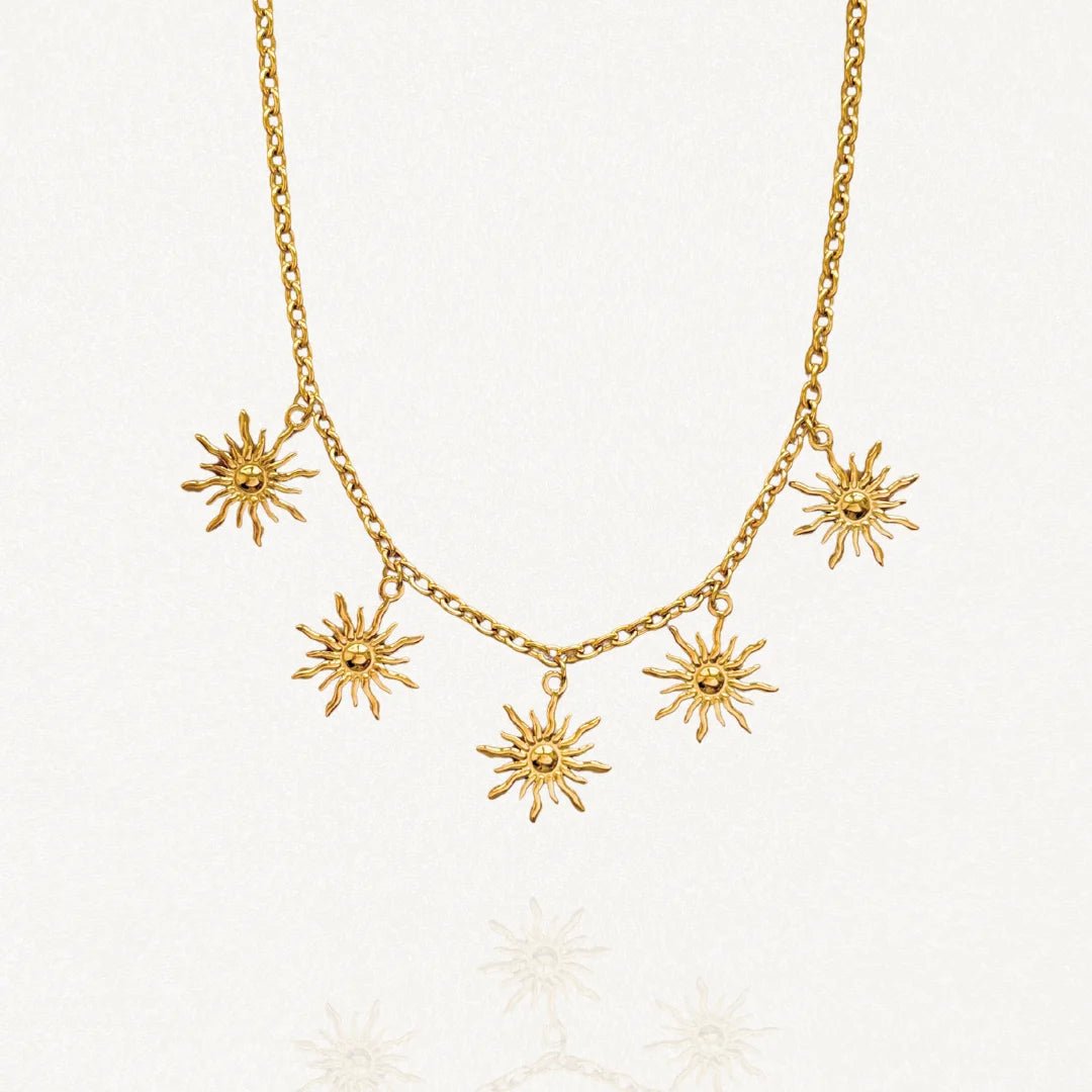 Vue d'ensemble collier chaîne dorée avec multiples pendentifs motifs solaires rayonnants sur fond blanc.
