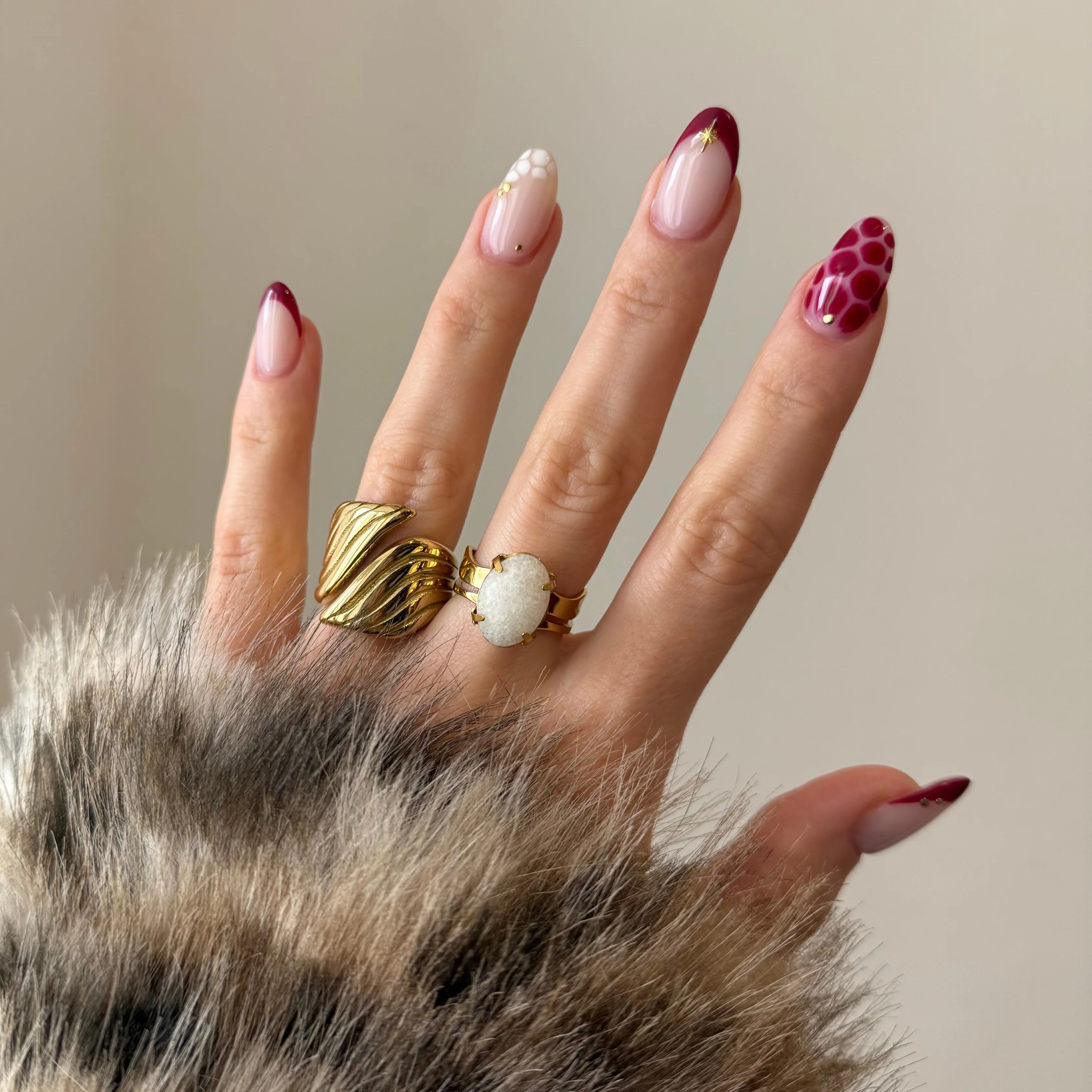Duo de bagues dorées portées à l'index et au majeur, mises en valeur par une manucure graphique rouge.
