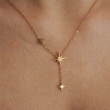Zoom sur le collier fin doré porté au cou : chaîne délicate et pampilles étoiles polaires, style minimaliste chic.