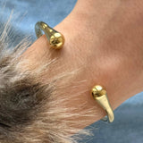 Gros plan sur les extrémités en forme de goutte du bracelet jonc doré porté au poignet, montrant la brillance du métal.