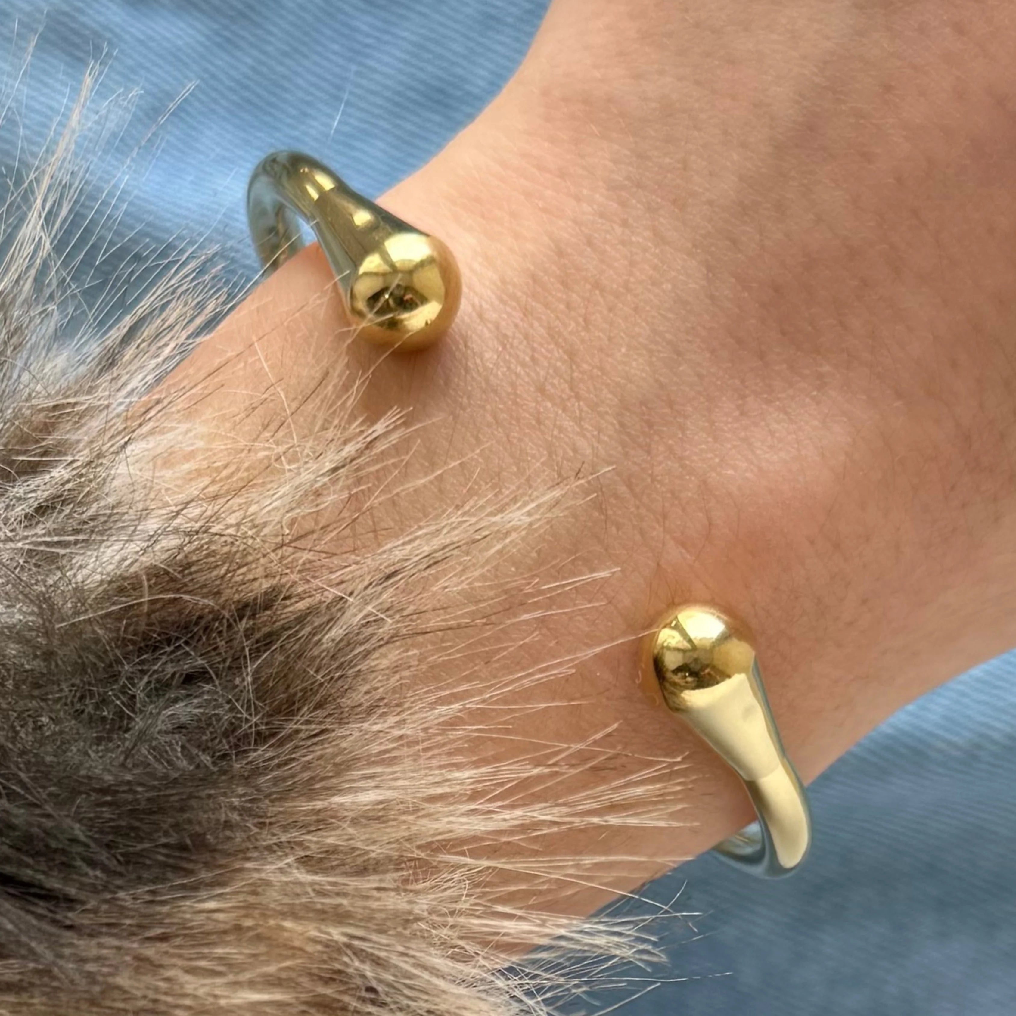 Gros plan sur les extrémités en forme de goutte du bracelet jonc doré porté au poignet, montrant la brillance du métal.