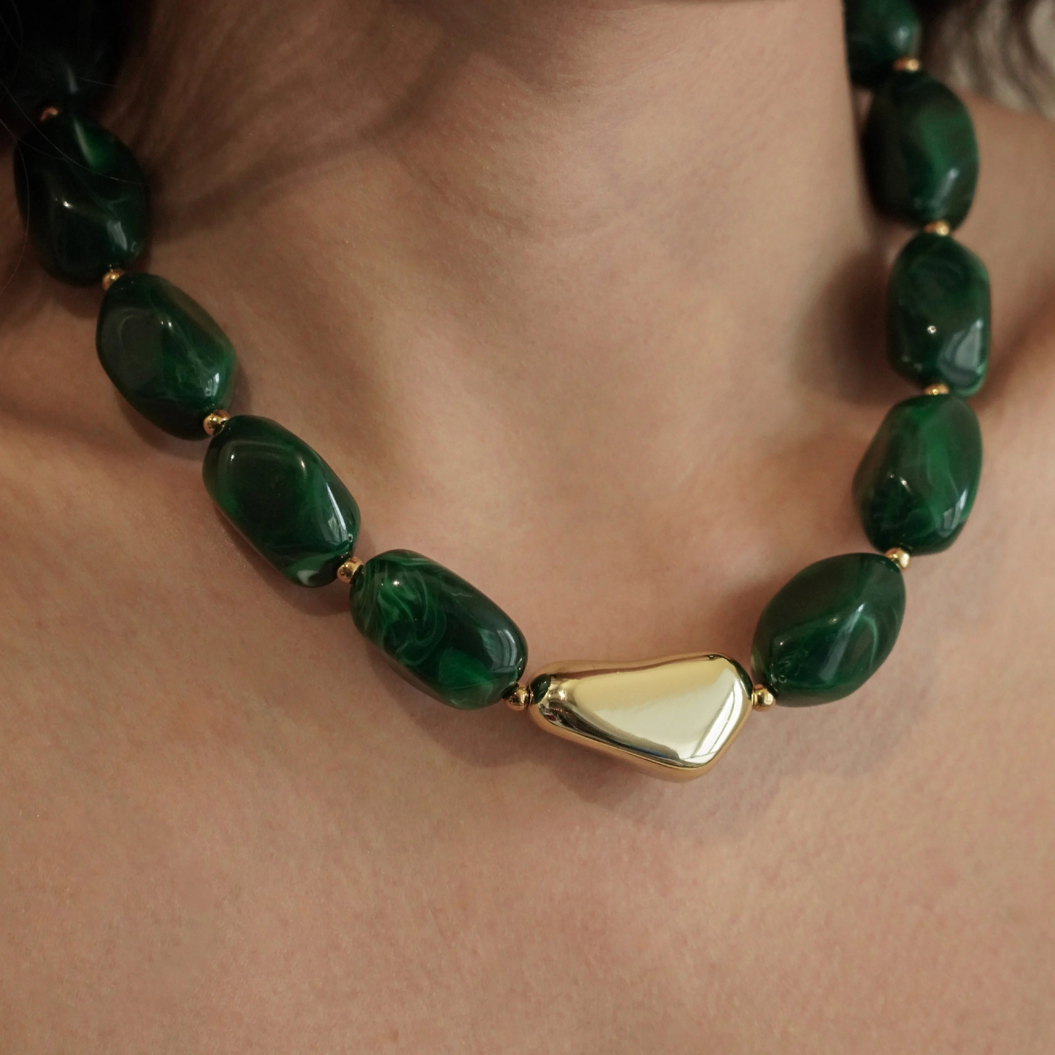 Gros plan sur le collier court MAISON DE L'AMOUR porté au cou, montrant les détails des perles vertes et le rendu sur la peau.