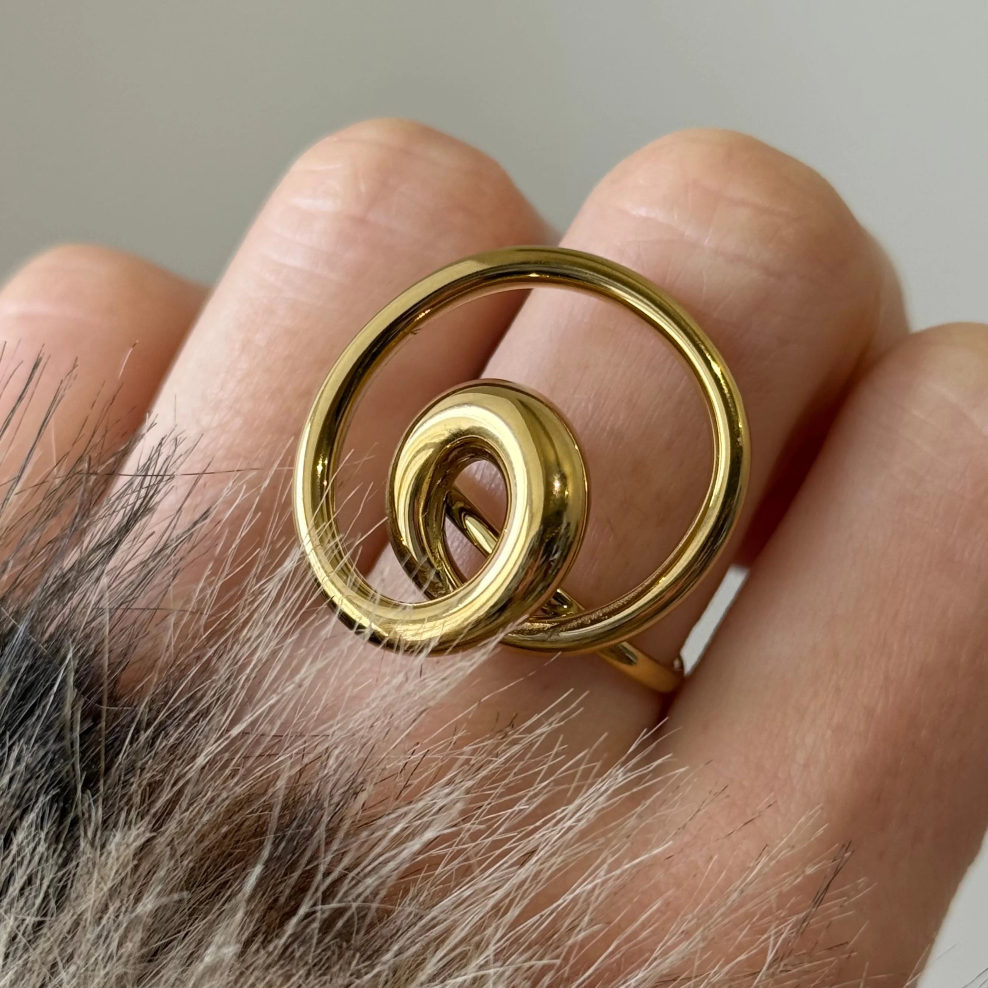 Bague statement dorée de forme ronde et spirale portée à l'annulaire.