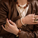 Tendance stacking : accumulation de colliers MAISON DE L'AMOUR avec une chaîne dorée à pendentifs cœurs et un collier perles marron.