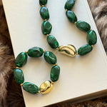 Ensemble collier et bracelet assorti MAISON DE L'AMOUR à perles vertes et détails dorés posés sur un livre, inspiration cadeau.