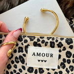Bague et bracelet jonc ouverts dorés disposés dans une trousse à motif léopard avec étiquette brodée Amour.