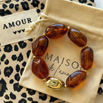 Bracelet perles ambre et or présenté sur sa pochette en tissu beige Maison de l'Amour et trousse léopard.