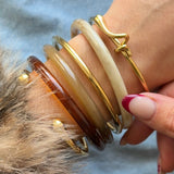 Accumulation tendance de bijoux au poignet : mélange d'un bracelet jonc doré à nœud et de joncs en résine colorée.