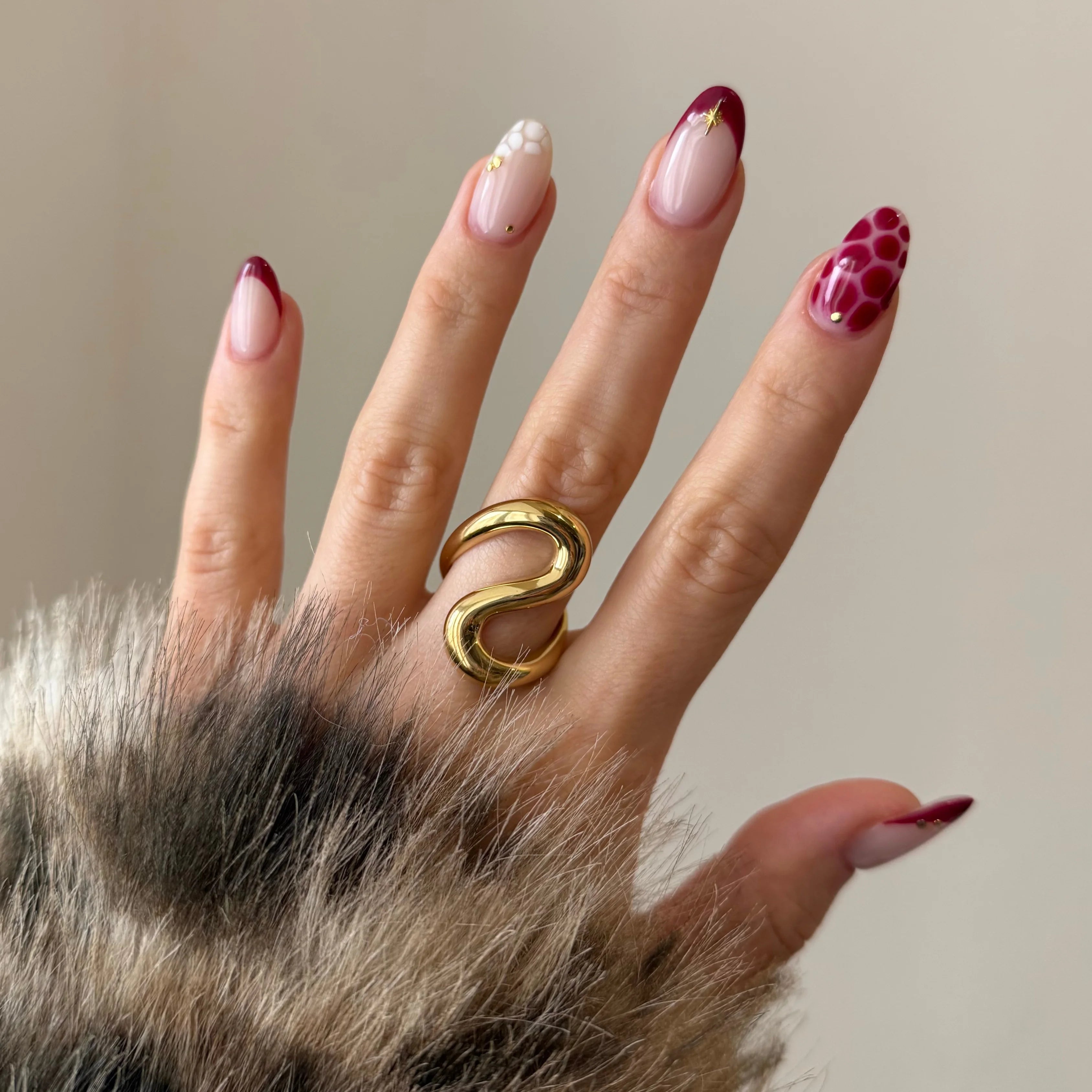 Bague dorée forme serpent abstrait portée au doigt, accessoire tendance associé à une manucure bordeaux et un manteau.