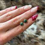 Mise en avant de la taille délicate des puces d'oreilles vertes et dorées tenues en main, avec manucure assortie.