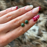 Mise en avant de la taille délicate des puces d'oreilles vertes et dorées tenues en main, avec manucure assortie.