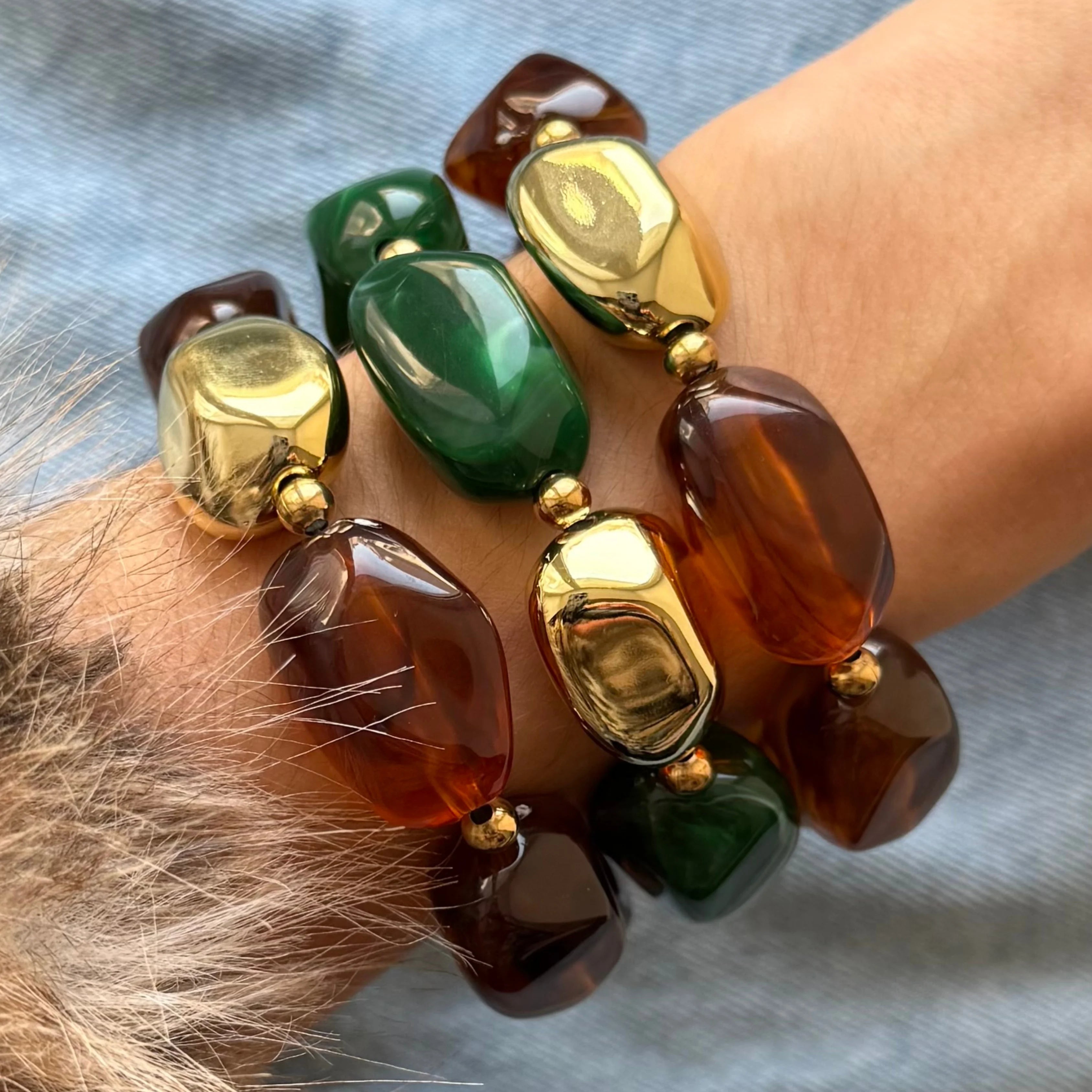 Accumulation de trois bracelets élastiques composés de grosses perles irrégulières en résine verte, marron effet écaille et dorée brillante.