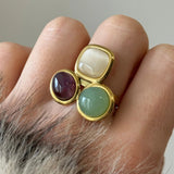 Gros plan sur une bague composée de trois pierres de couleurs différentes portée au doigt, montrant le volume des cabochons.