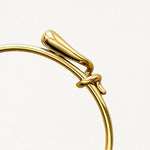 Gros plan sur le détail du nœud entrelacé et la finition lisse du bracelet jonc doré.