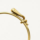 Gros plan sur le détail du nœud entrelacé et la finition lisse du bracelet jonc doré.