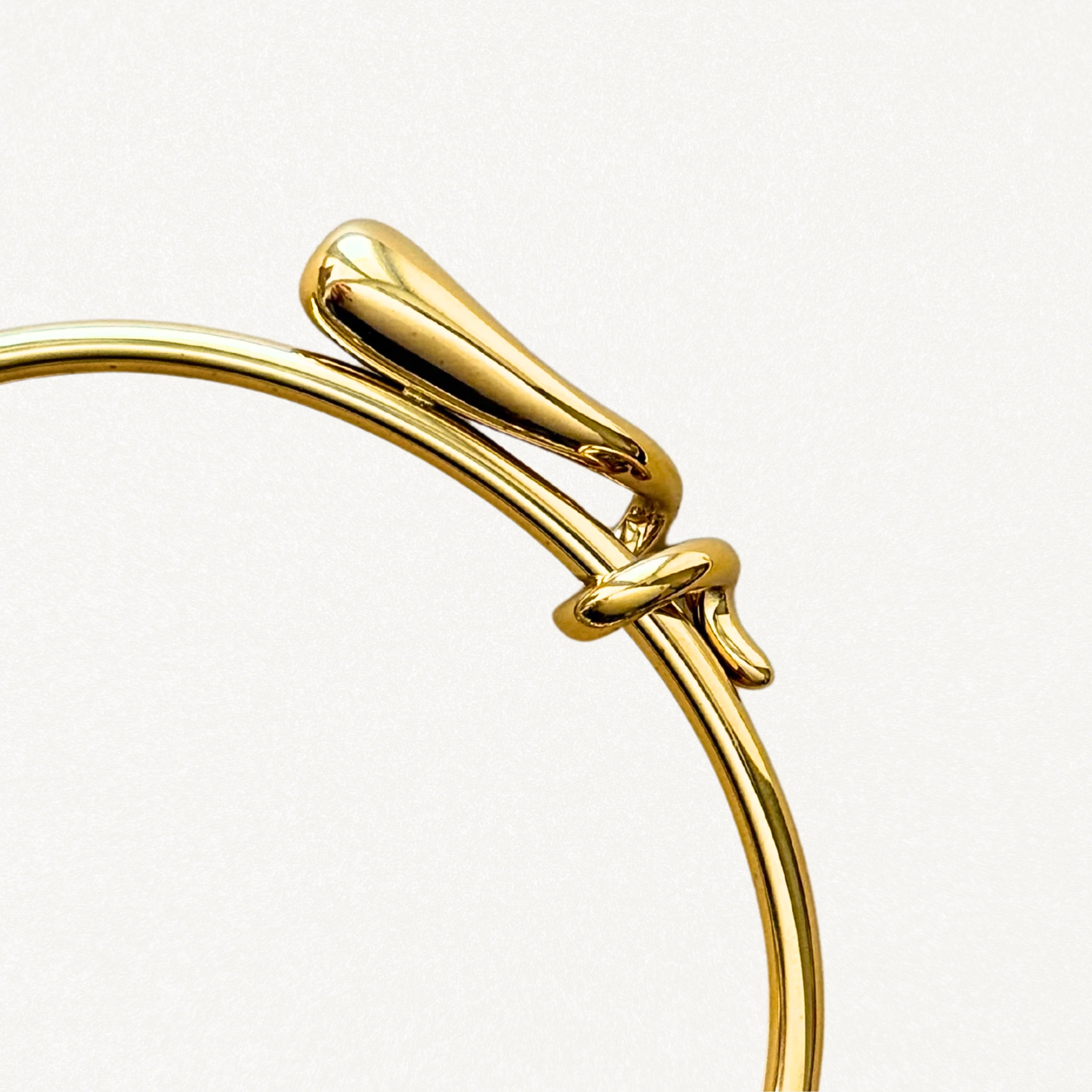 Gros plan sur le détail du nœud entrelacé et la finition lisse du bracelet jonc doré.